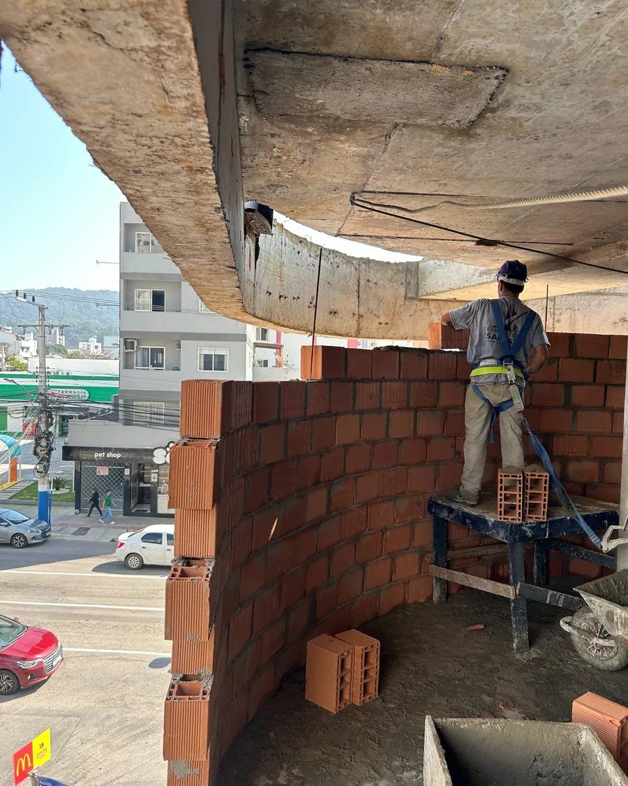 Colaborador executando alvenaria sobre cavalete, em pavimento aberto para a rua