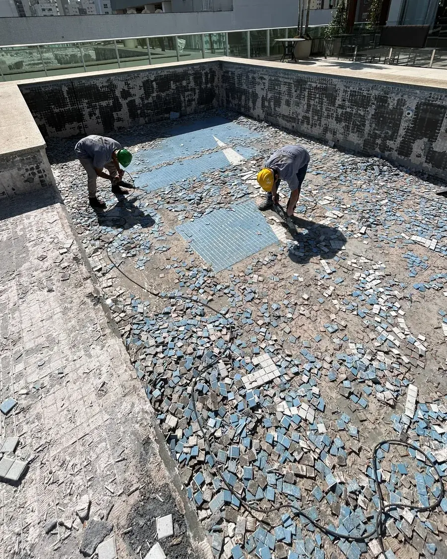 Dois colaboradores removendo o revestimento antigo de uma piscina drenada