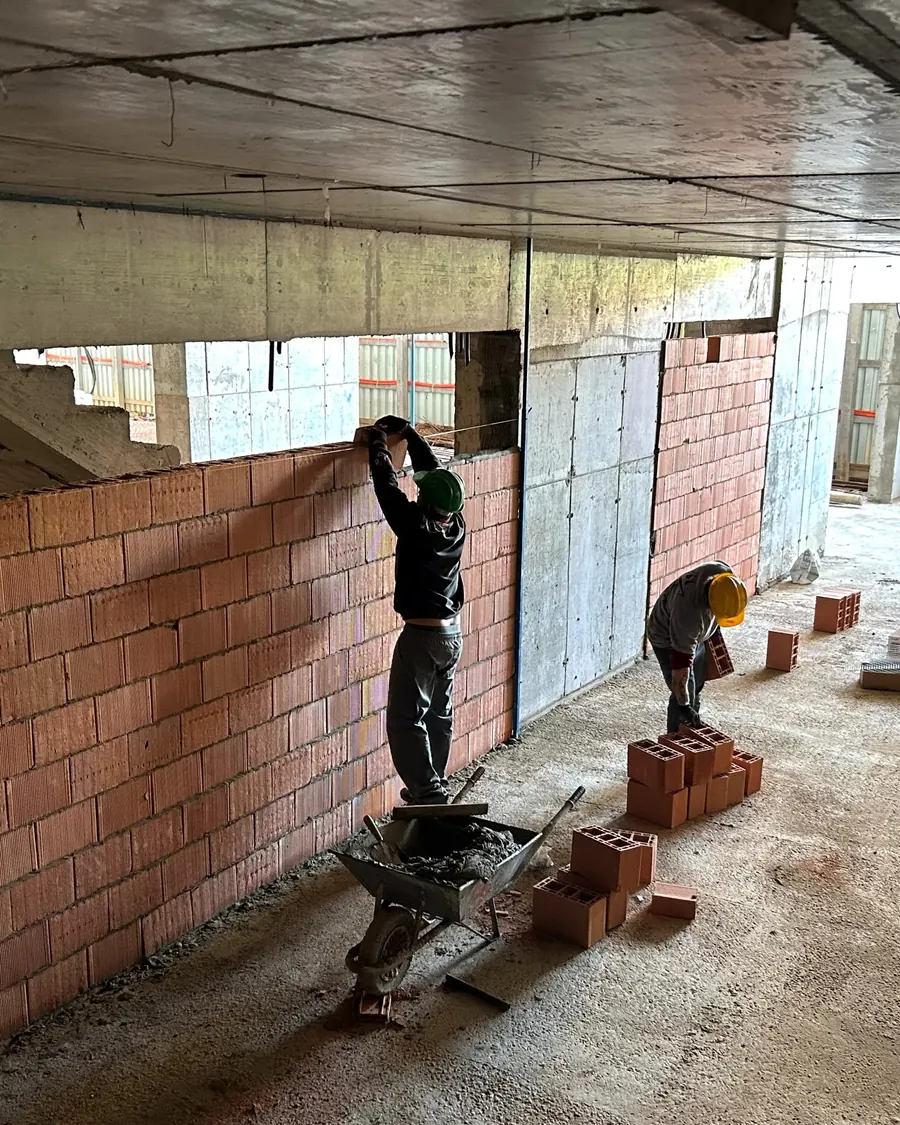 Dois colaboradores assentando blocos cerâmicos em pavimento tipo, um deles sobre cavalete
