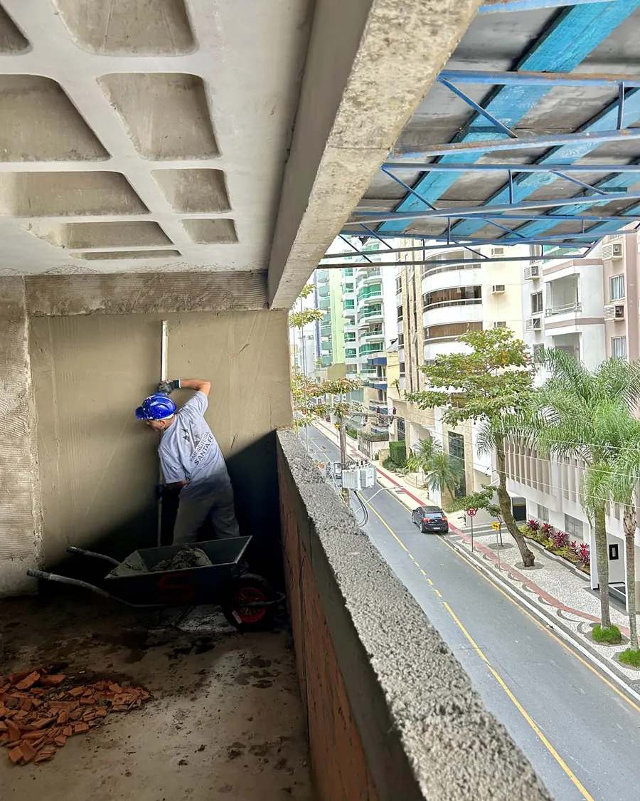 Colaborador aplicando argamassa em parapeito de sacada, com a avenida ao fundo